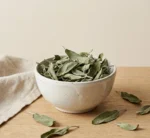 Dried sage leaves in handmade ceramic bowl on warm beige background with soft daylight