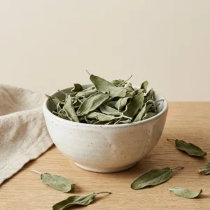 Dried sage leaves in handmade ceramic bowl on warm beige background with soft daylight