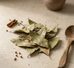 Whole bay leaves with cinnamon stick and coriander seeds on warm stone surface