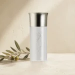 Hero Image: Assaf Aura Eau de Parfum for Men 150ml bottle on a warm neutral limestone background with a delicate olive branch and soft natural daylight.