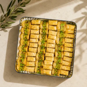 Traditional pistachio baklava fingers arranged in a tray with golden flaky pastry layers and premium pistachio filling on a warm neutral background.