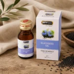 Hemani Black Seed Oil 30ml bottle with original retail box displayed on natural oak wood with black seeds and soft linen details.