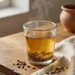 Jordanian anise tea infusion in a glass cup beside whole anise seeds on a warm oak table with natural linen and soft daylight.
