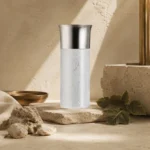Base Notes Image: Assaf Aura Eau de Parfum for Men 150ml with patchouli leaves, brushed brass accents, ivory fabric, and warm mineral textures inspired by ambergris and musk.