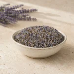 Premium Lavender Flowers in a handcrafted ceramic bowl on a natural limestone surface with softly blurred lavender stems, warm daylight and minimalist botanical styling.